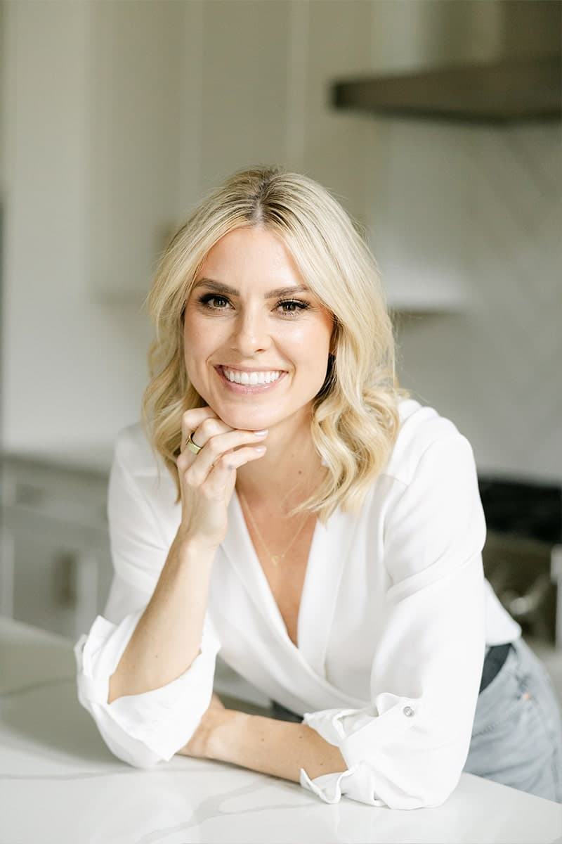 Keeli smiling warmly with her chin resting on her hand in a kitchen.